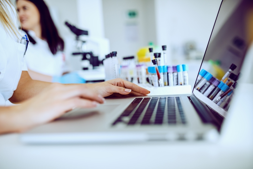 A close-up of a woman typing on her laptop, building a report using a specific lab reporting format.